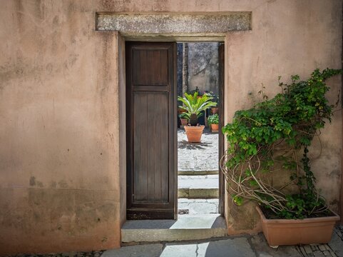 Inviting Mediterranean travel photograph showing a peek into a quiet green courtyard through an open doorway in Erice, ideal for Sicilian lifestyle guides and travel media.