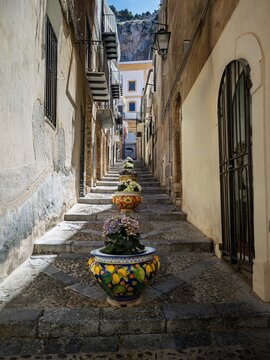 Charming Mediterranean travel photograph of a decorated stone staircase lined with colorful ceramic pots in historic Cefal&ugrave;, ideal for Sicilian travel guides and lifestyle media.