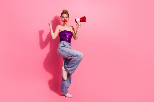 Energetic Young Woman in Fashionable Attire Holding Megaphone Amidst Splashy Pink Background