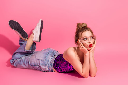 Trendy woman lying on pink background in fashionable outfit, expressing happiness and confidence in a modern style