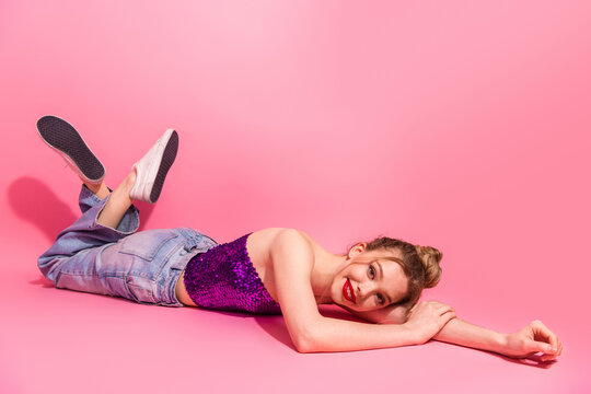 Fashionable young woman in casual chic style lying on pink background wearing shiny sequined top