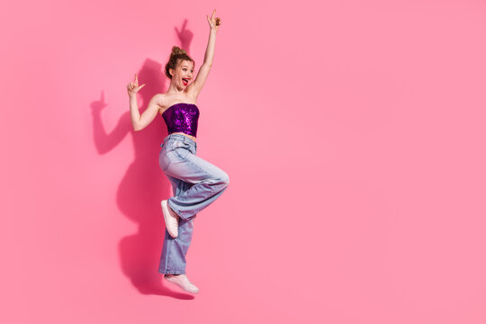 Young woman in shiny sequin top jumping joyfully on pink background embodying youthful energy and stylish expression