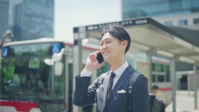 Smiling businessman talking on the phone while waiting for a bus