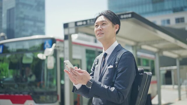 Businessman checking his smartphone while waiting at a bus stop
