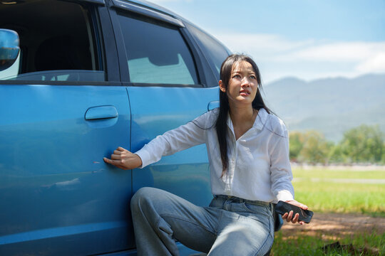 Asian woman pointing at car door scratch while calling assistance