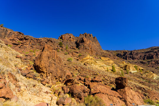 Colorful volcanic rock formations and steep mountain slopes of Los Azulejos de Veneguera under a clear blue sky in Gran Canaria, Canary Islands.