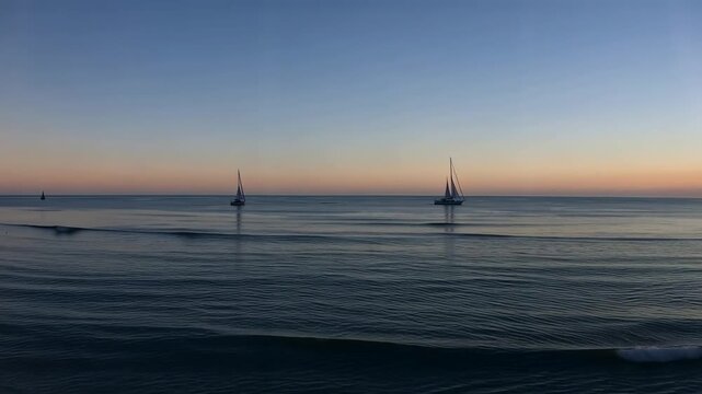 Sailboats anchored in calm ocean at sunset with gradient sky and gentle waves lapping shore