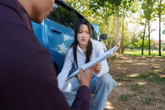 Asian woman showing claim document to car insurance agent outdoors