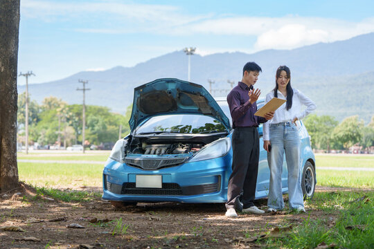 Insurance agent reviewing claim form with driver by broken blue car