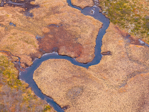 Aerial view of a winding river flowing through a marshy landscape with autumnal brown grasses and moss in Fjord, More og Romsdal, Norway.