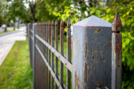 Weathered Metal Fence with Rusty Spikes Along a Green Urban Street