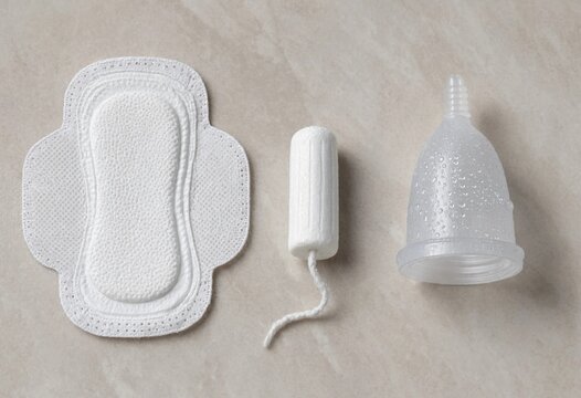 A selection of various feminine hygiene products including a sanitary pad, a tampon, and a reusable menstrual cup on a neutral background