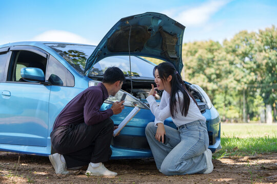 Insurance agent inspecting broken car engine with woman driver outdoors