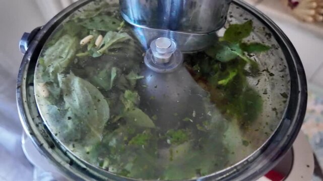 4K footage of a blender grinding basil and pine nuts in slow motion to make Genoese pesto for a Mediterranean diet. Ideal for cooking classes and diet-related content.