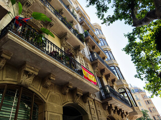 Sunny historic Barcelona Spain apartment building with ornate balconies, wrought iron railings and a Spanish flag above a tree lined street © AS Photo Family