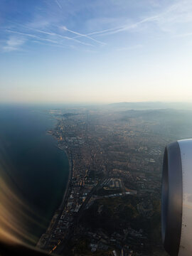 Aerial view of a coastal city from airplane window showing jet engine, coastline and urban landscape at sunset