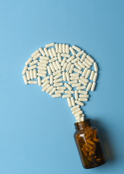 White supplement capsules form human brain shape above amber bottle on blue background for memory, focus and cognitive health concepts.