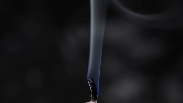Close-up of white smoke rising from an extinguished candle wick. Swirling smoke trail against a dark background in slow motion. Abstract mystery and ending concept