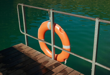 Orange life buoy hanging on a dock railing over a green alpine lake, close-up © Pablo
