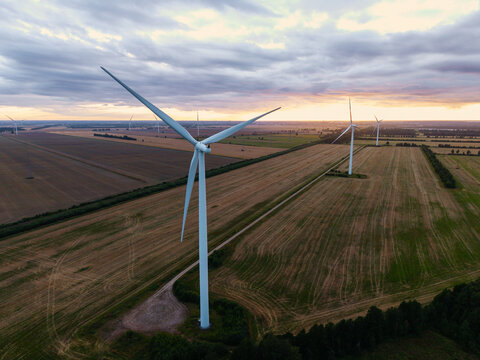Aerial view of Targale Wind Park with large wind turbines standing in agricultural fields under a dramatic sunset sky in Targale, Ventspils Municipality, Latvia.