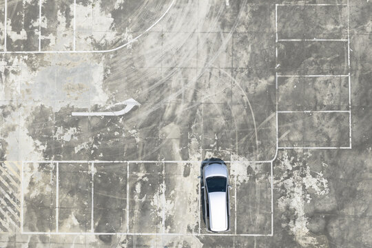 Aerial view of a silver car parked in a weathered concrete parking lot with visible tire marks and painted lines in Taiwan.