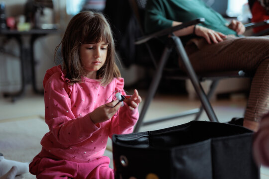 
Little Girl In Pink Sweater Playing Near Her Family Member. Focused child examines a small toy while sitting by an adult indoors
