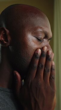 Agonized African American individual shielding lips with fingers near domestic window frame, enduring silent panic, severe emotional trauma, and heartbreak