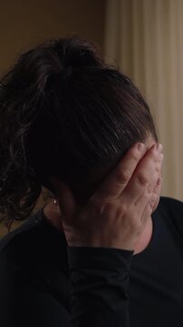 Grieving adult female shielding face with open palms near domestic window frame enduring acute psychological breakdown and helpless isolation