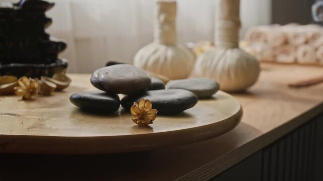 Basalt massage stones and herbal compress balls resting on wooden tray with rising incense smoke. Footage suitable for advertising wellness centers, aromatherapy, or holistic bodycare services