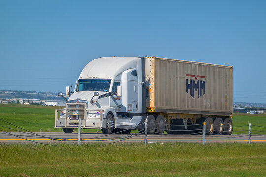 Calgary, AB, Canada - Sept 16, 2026: White semi-truck hauling an HMM shipping container along a prairie highway on a sunny day.