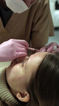 A masked cosmetologist holds a syringe and injects botox into a client's forehead skin near the eyebrow, top-down view