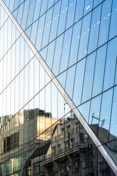 Reflective glass facade in London England mirrors older architecture creating layered contrast between modern office design and historic city buildings