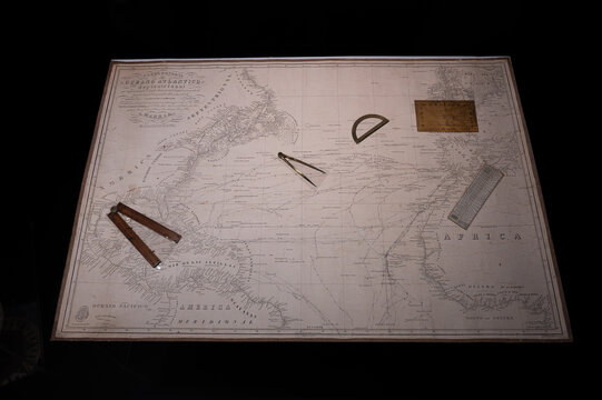 Nautical chart of the North Atlantic Ocean with vintage navigation tools including brass dividers, protractor, and ruler on a dark background.