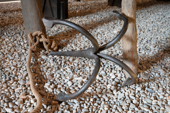 Vintage four-pronged grapnel anchor with rope lying on a stony pebble bed.
