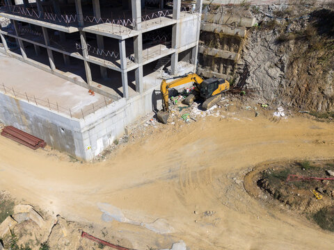 Aerial view of an excavator working at a construction site with a concrete building frame and dirt ground in Istanbul, Istanbul, Turkiye.