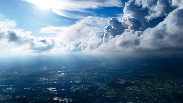 Aerial view of the lush green landscape and residential areas under dramatic clouds with sun rays breaking through in Sukabumi Regency, West Java, Indonesia.