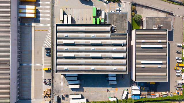 Aerial view of the EcoEridania S.p.A. industrial facility featuring large warehouses with corrugated roofs, loading docks, and parked trucks, San Giuliano Milanese, Lombardia, Italy.