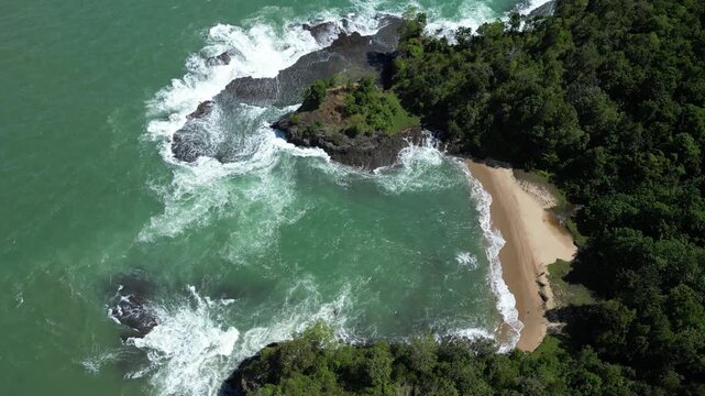 Calang, Indonesia: Slow motion tilt down aerial drone footage of wave breaks into rocky coastline by the beach in bay of Calang, coastal town in Aceh Jaya of Sumatera, Indonesia surrounded by tropical