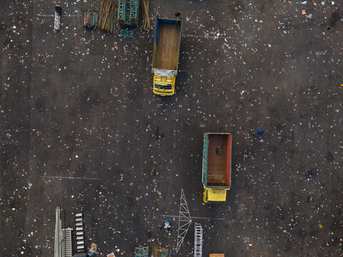 Aerial view of two yellow trucks parked on a large industrial lot with scattered construction debris and materials in Purwokerto, Central Java, Indonesia.
