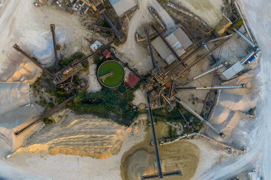 Aerial view of an industrial quarry site featuring complex conveyor belt systems, a circular settling pond, and large piles of processed aggregate in Rome, Lazio, Italy.