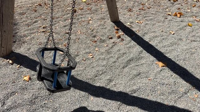Empty wooden playground swing gently moves back and forth on two metal chains outdoors, creating a quiet childhood and recreation scene without people.
