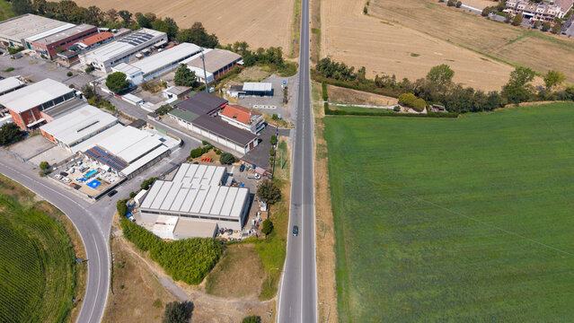Aerial view of industrial buildings and warehouses situated along a road adjacent to agricultural fields in Zona Artigianale S.P. 157, Lombardy, Italy.