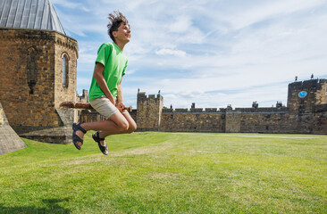 Fototapeta premium Teen have fun joyfully jumping on broomstick in castle courtyard