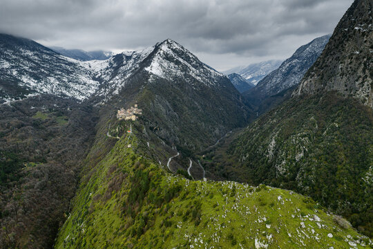 Aerial view of the mountain village of Castrovalva perched on a rocky ridge surrounded by snow-capped peaks and lush green slopes in Anversa degli Abruzzi, Abruzzo, Italy.