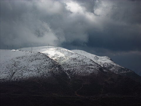 Aerial view of snow-covered mountains with communication towers under a dramatic stormy sky in Anversa degli Abruzzi, Abruzzo, Italy.