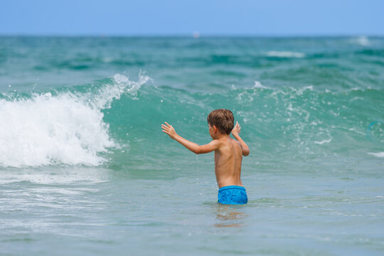 Boy have fun wading through ocean waves on sunny resort