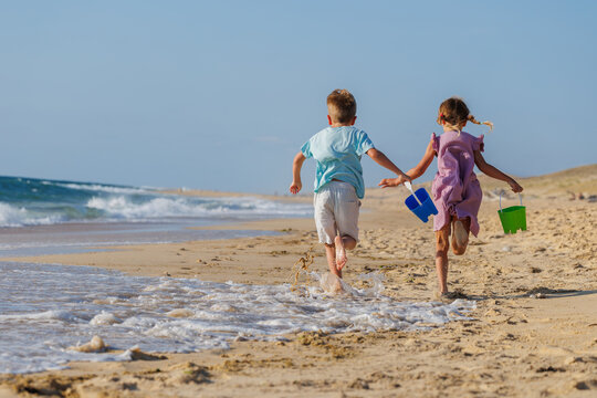 Boy and girl running along a sandy beach carrying toy buckets