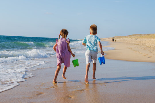 Happy kids boy and girl run in sunset ocean beach with buckets