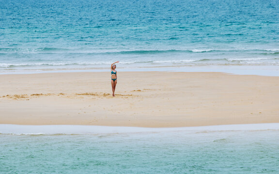 Woman waving hand while standing on a sandy island in the ocean