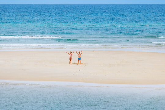 Children boy and girl raise arms together on small sandy island